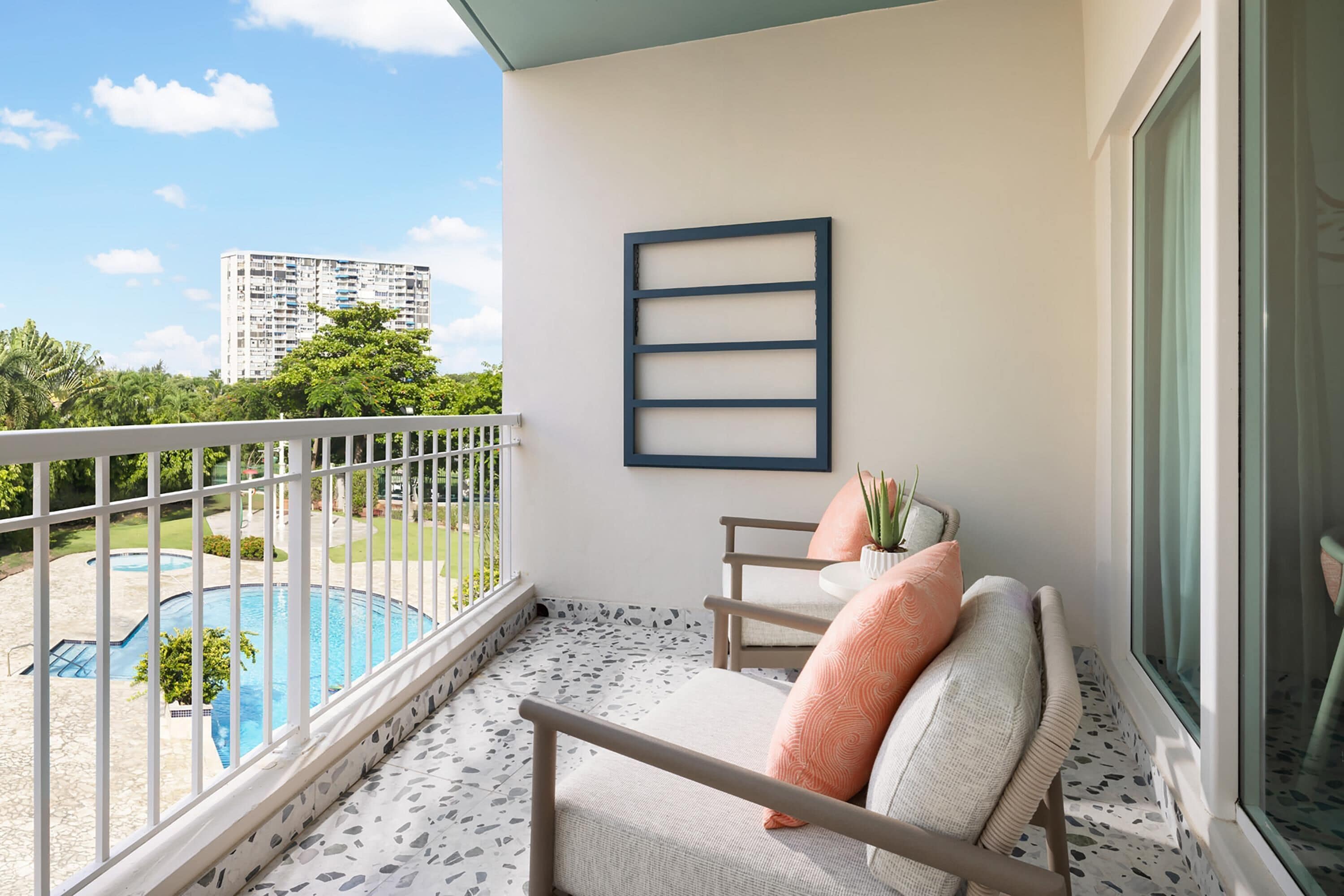 A balcony with a pool view, a framed artwork, and a seating area with cushions.