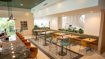 Un café moderno con una barra larga, varias zonas de estar y plantas de interior.