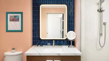 Un baño con lavamanos blanco, espejo, ducha y retrete.