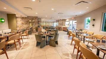 A spacious dining area with multiple tables and chairs, a counter, and a view of the outside through large windows.