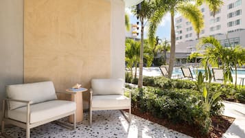 Un espace de détente extérieur moderne, avec deux chaises et une petite table, entouré d’une végétation luxuriante et d’une piscine.