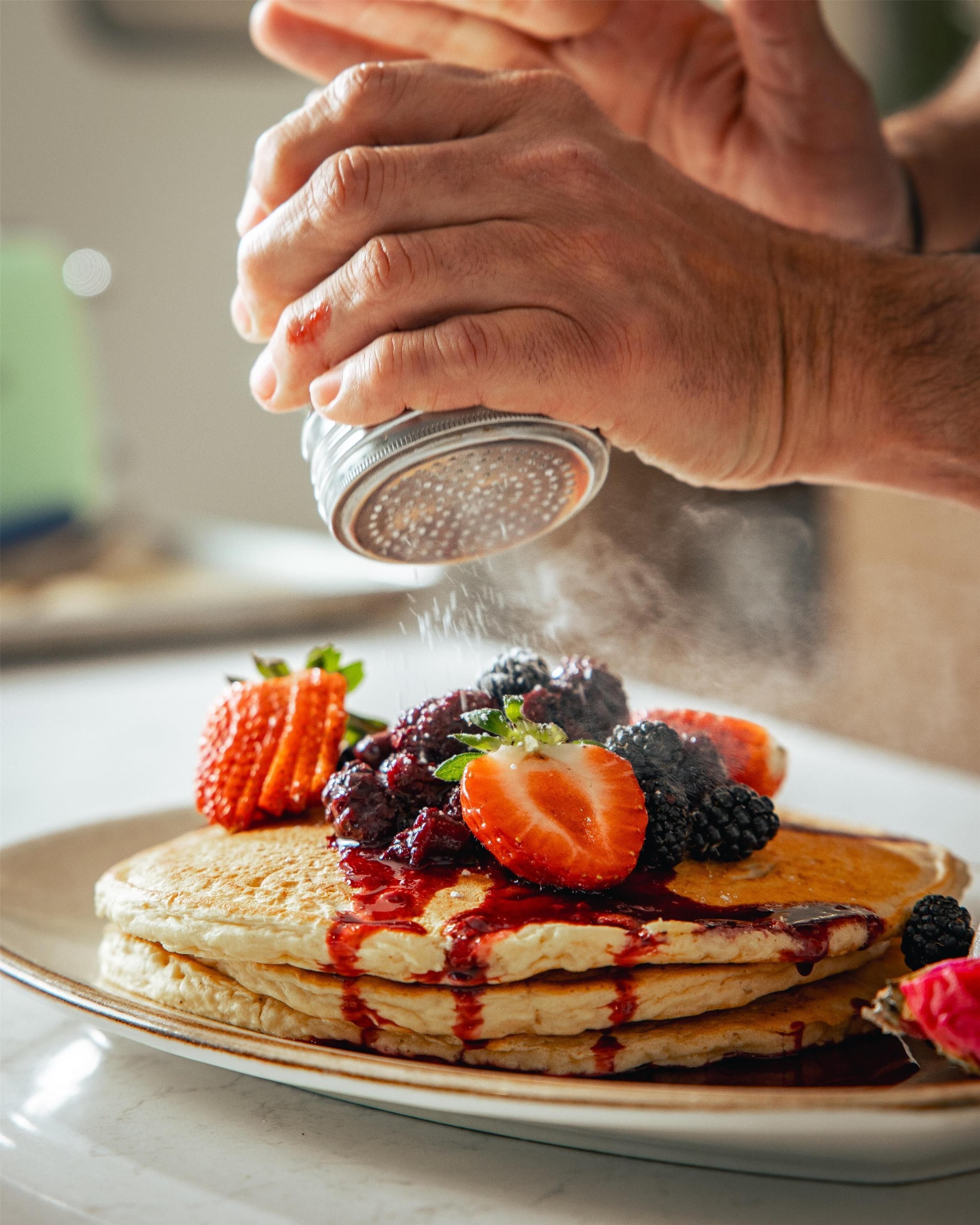 Une pile de crêpes garnie de fruits rouges et nappée de sirop, présentée sur une assiette.