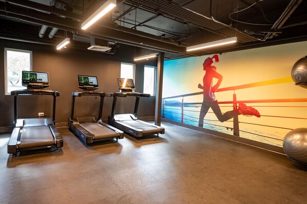 A gym with treadmills, a large screen displaying a boxing match, and a view of the sea through large windows. - Hyatt Centric San Juan - Isla Verde (Carolina)
