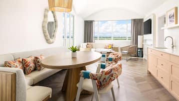 Una habitación de hotel moderna con una mesa redonda de comedor, sofá, sillones, televisión y vistas a la ciudad.