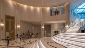 Un hall espacioso con una imponente escalera, una zona de recepción y un alto techo con tragaluces.