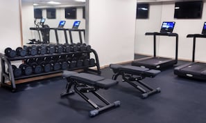 A gym with treadmills, dumbbells, and weight benches.