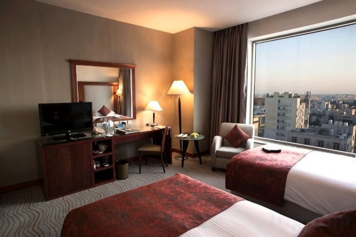 A hotel room with a bed, a desk, a television, a chair, and a large window offering a city view.