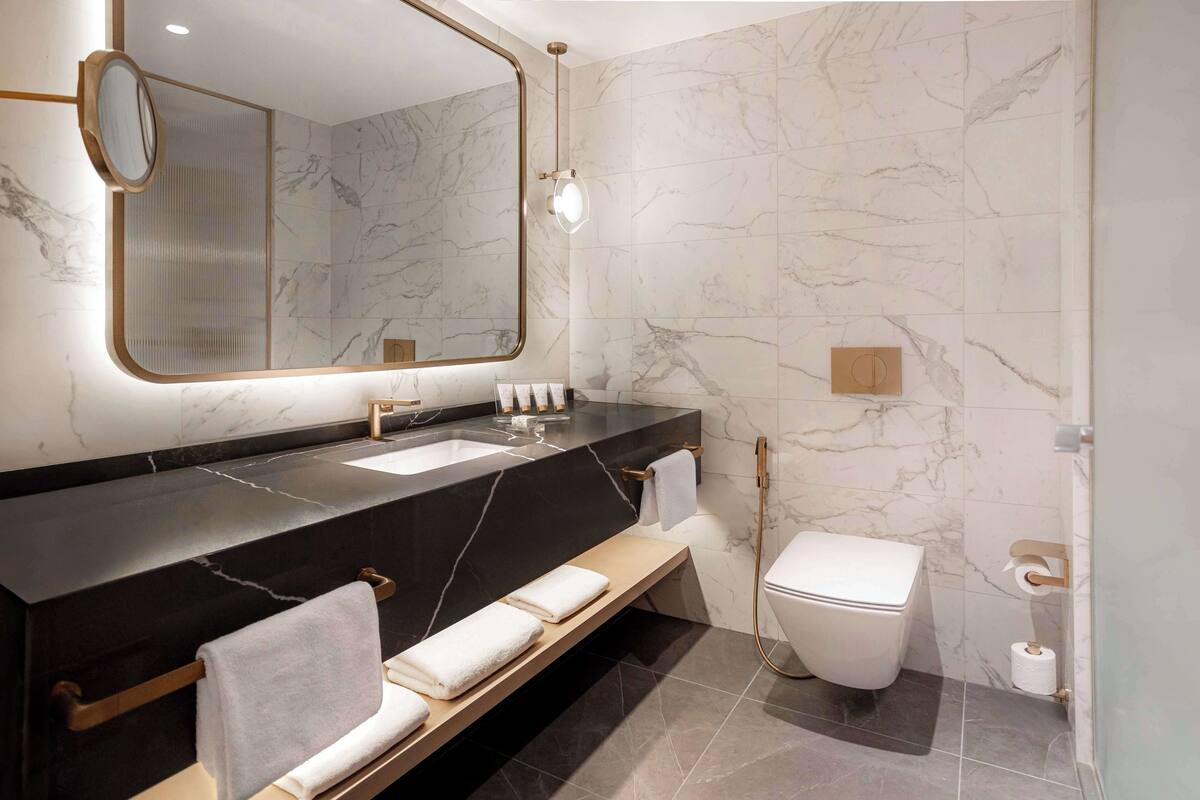 Ein modernes Badezimmer mit Marmorwand, schwarzem Waschtisch, Waschbecken, Toilette und einer Sitzbank mit Handtüchern.