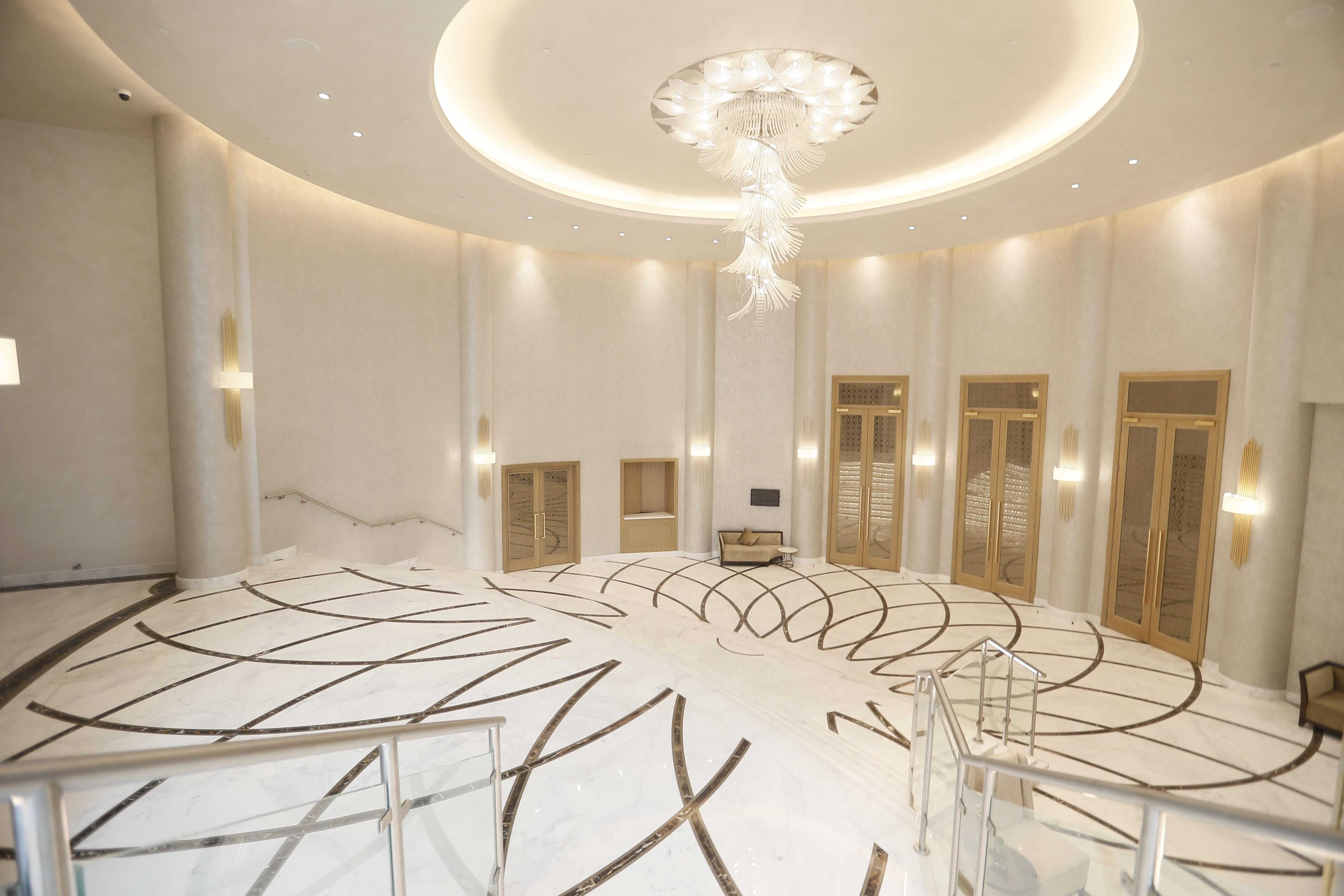 A spacious lobby with a central staircase, a chandelier, and a seating area.