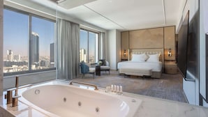 Una habitación de hotel moderna con una bañera grande, una cama, una zona de estar con vistas a la ciudad y un televisor.