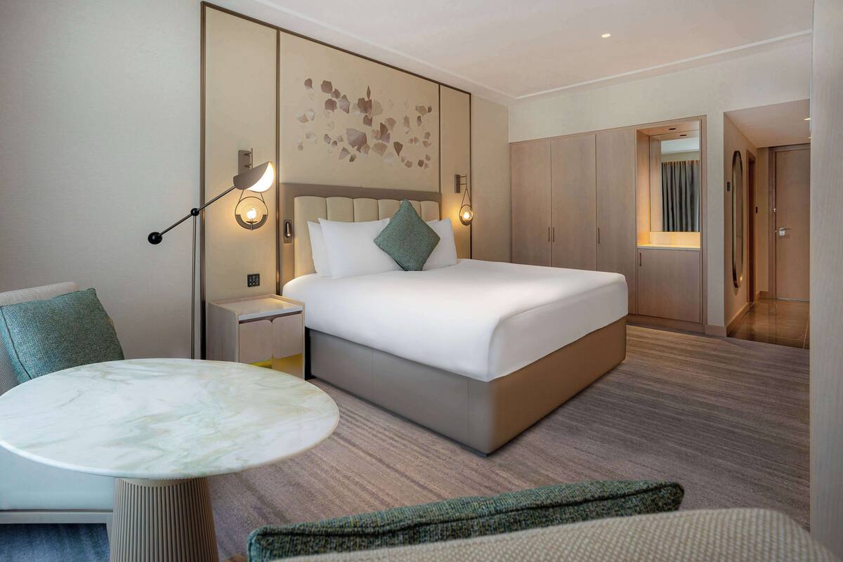 Ein modernes Hotelzimmer mit einem großen Bett, einem Nachttisch, einem runden Marmortisch und einer Wandleuchte.