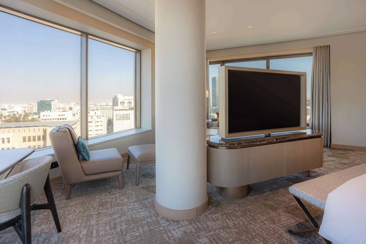 Ein modernes Hotelzimmer mit großem Fenster, Flachbildfernseher, Sofa, Sessel und Bett.