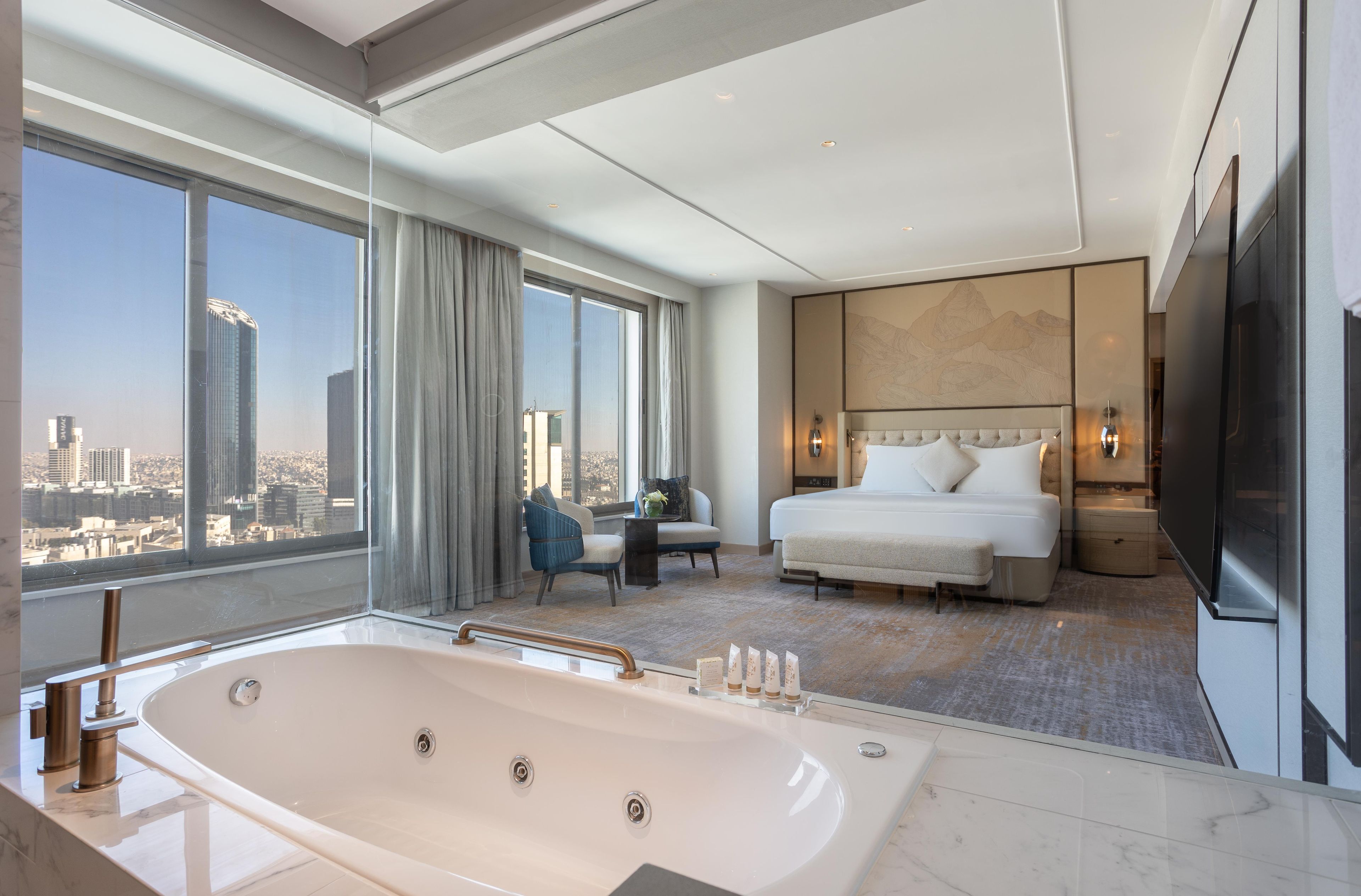 Una habitación de hotel moderna con una cama grande, zona de estar, bañera y vistas a la ciudad.