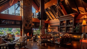 A spacious lounge with a fireplace, comfortable seating, and a bar area with shelves of bottles. - Anantara Golden Triangle Elephant Camp & Resort (Chiang Saen)