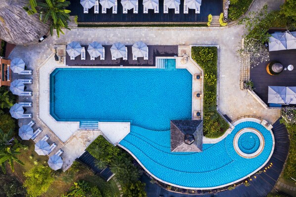 Una amplia piscina rectangular con un elemento espiral, rodeada de sillones de descanso y sombrillas.