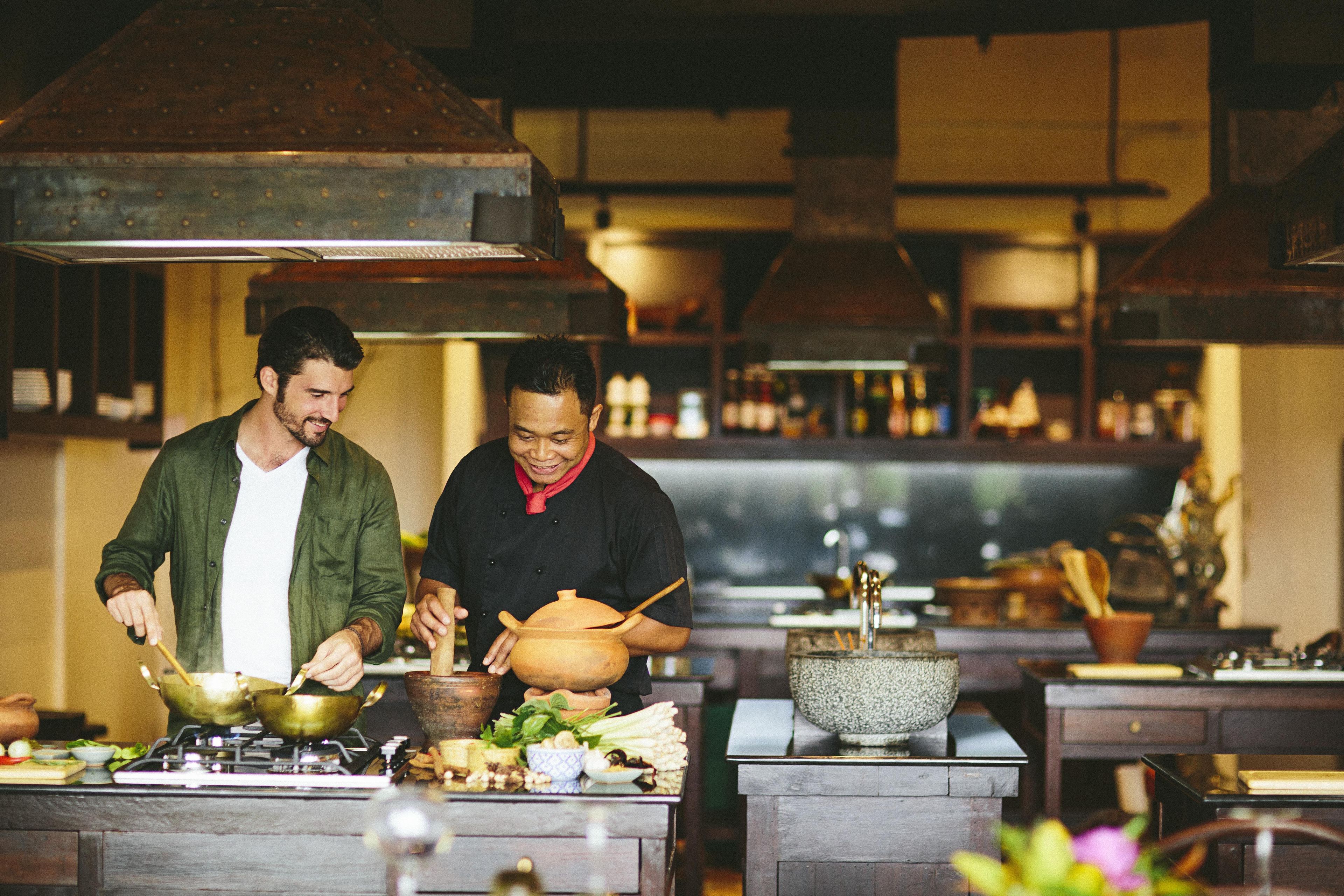 A kitchen with two chefs preparing food, various cooking utensils, and ingredients on the counter.
