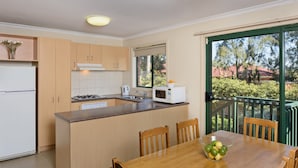 A modern kitchen with wooden cabinets, a built-in stove, a microwave, and a dining area with a table and chairs.