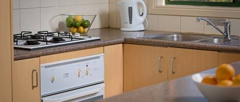 A kitchen with a gas stove, oven, and a kettle on the countertop.