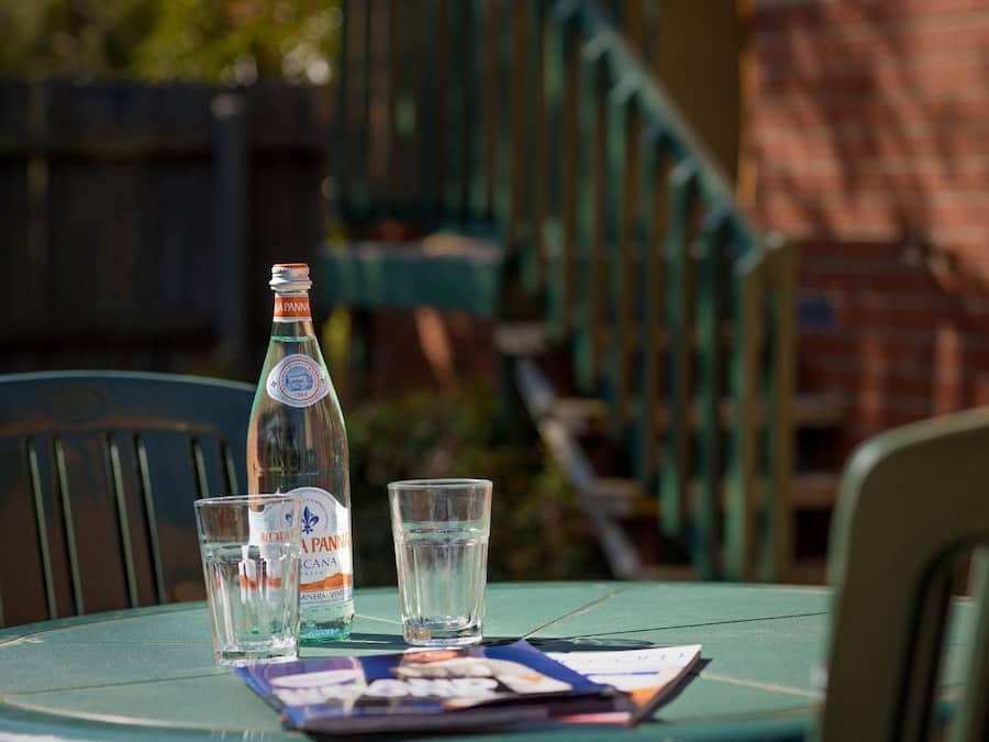 Una mesa con una botella, dos vasos, una revista y una silla.