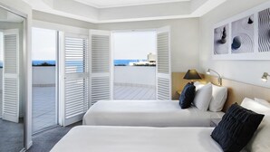Habitación de hotel con dos camas, vista al mar y una pared con tres obras de arte abstracto.