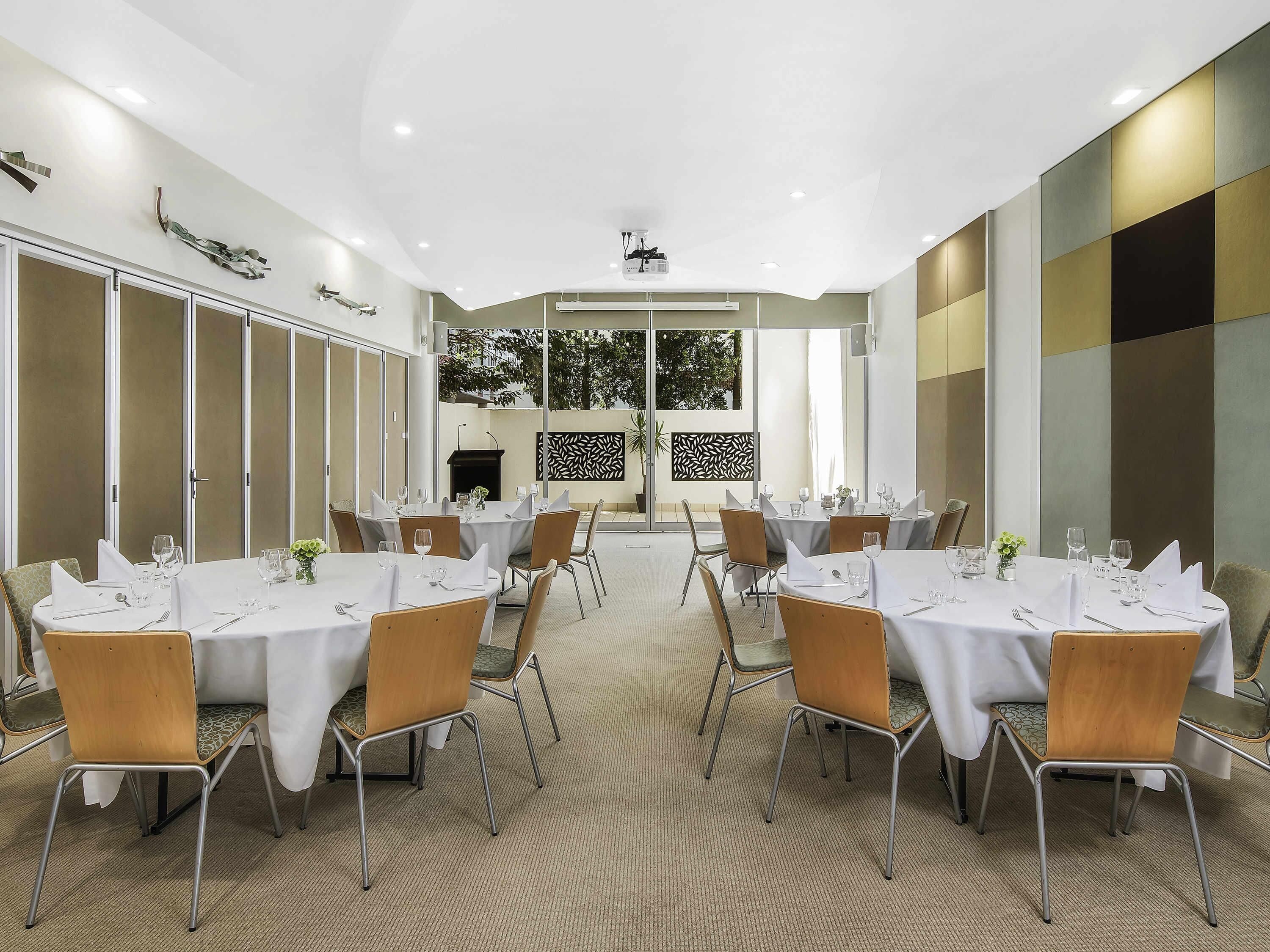 A conference room with round tables, chairs, and a projector screen.