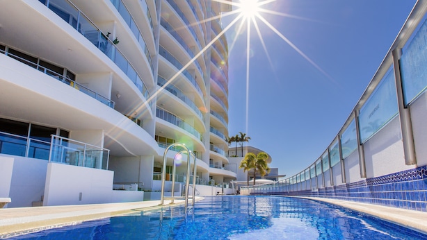 Un hotel moderno con piscina, varios balcones y cielos azules despejados.