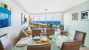 Un comedor con vista al océano, una mesa de vidrio y un conjunto de asientos.