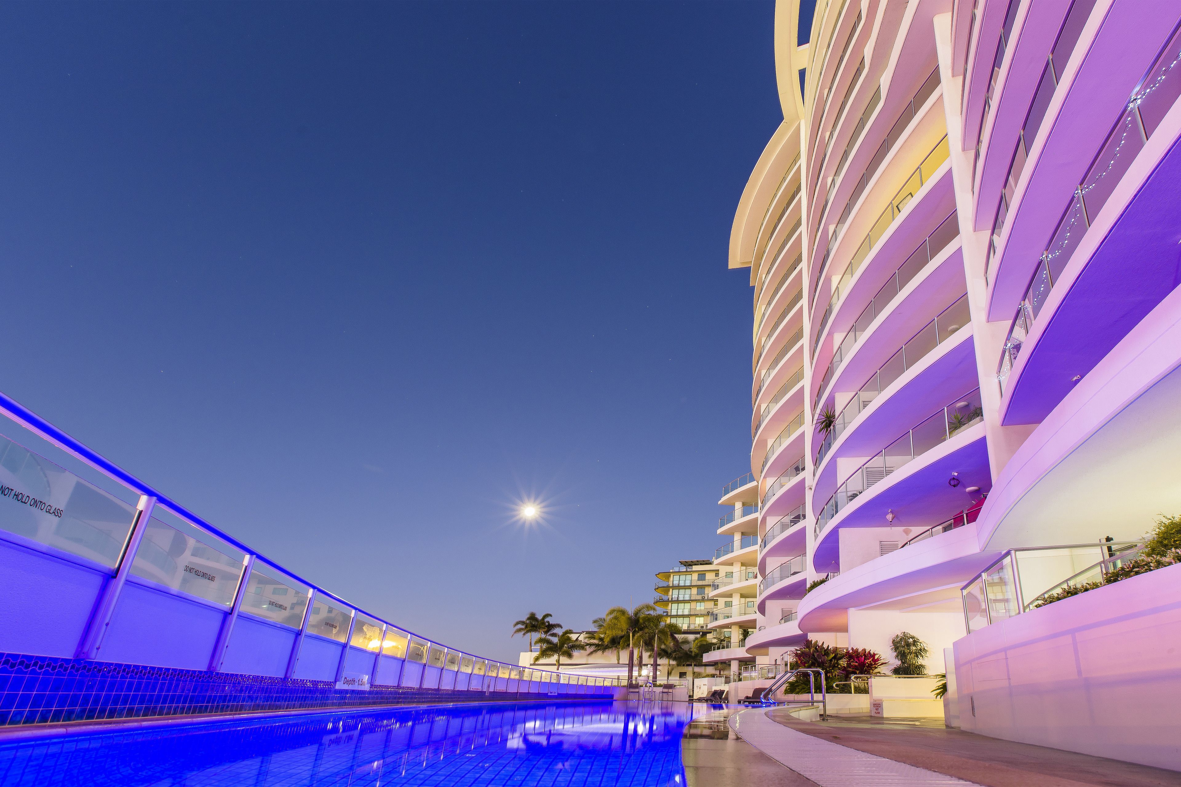 Um hotel moderno com área de piscina, várias varandas e vista desobstruída do céu noturno.