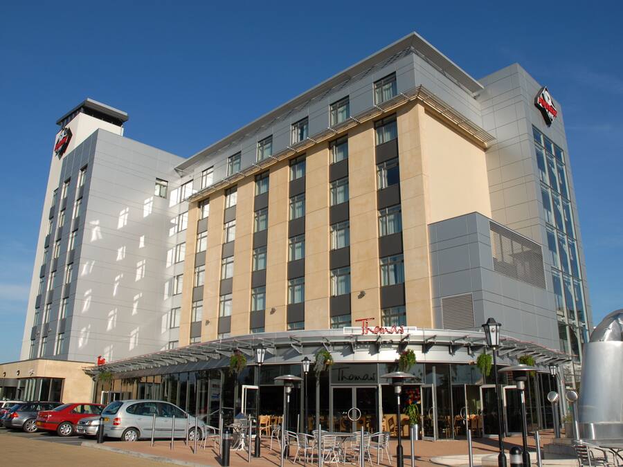 A modern hotel with a flat facade, multiple windows, and a covered outdoor seating area with tables and chairs.