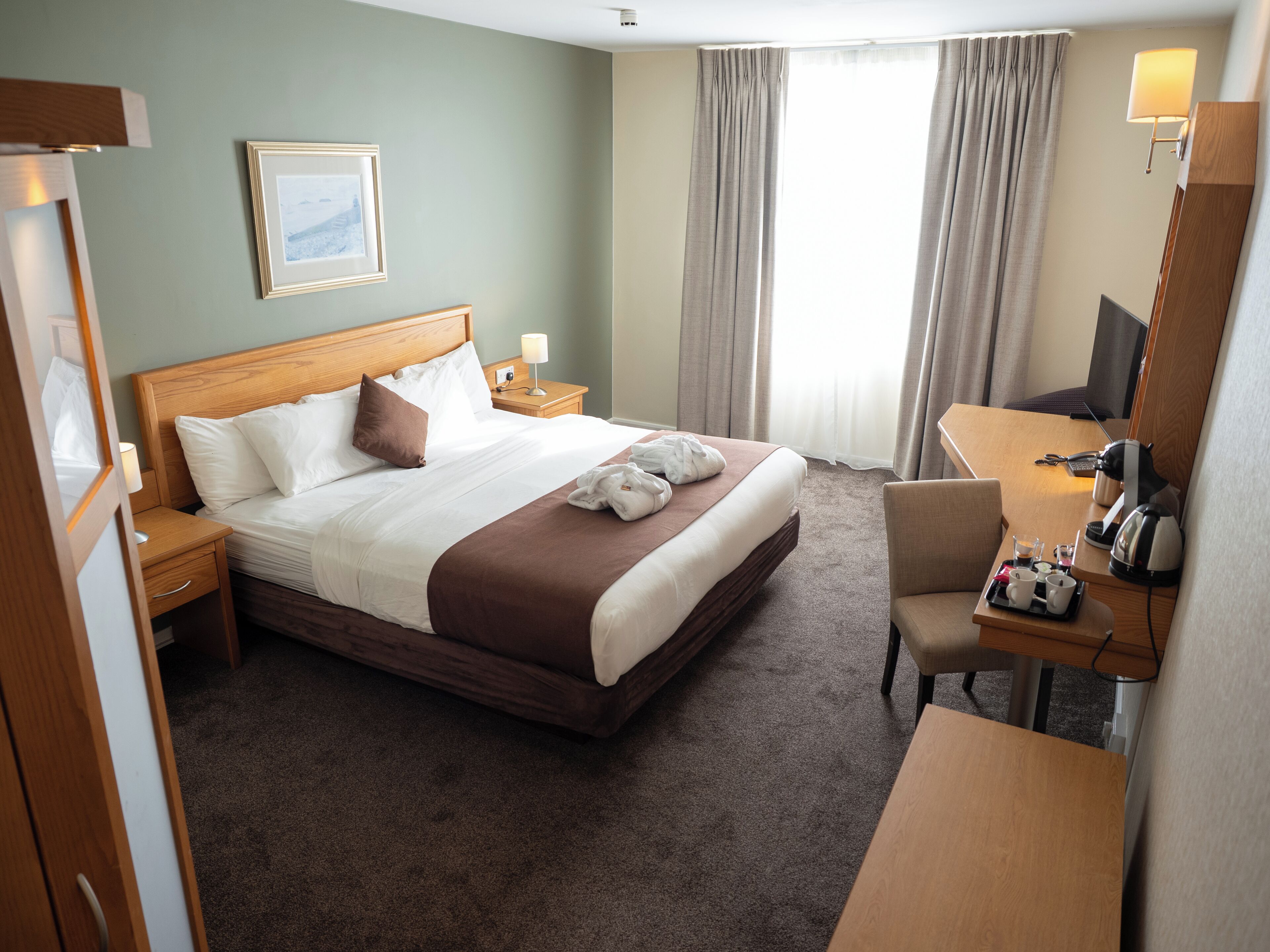 A hotel room with a large bed, a desk with a chair, a television, and a window with curtains.