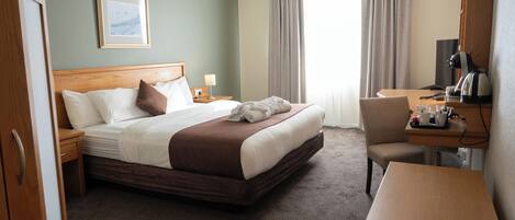 Une chambre d’hôtel avec un lit, un bureau, une chaise, une lampe et un tableau au mur.