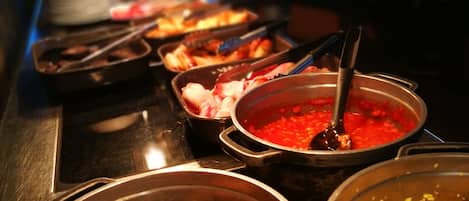 A buffet with various dishes including a pot of red sauce, a bowl of mushrooms, and a dish with yellow rice.