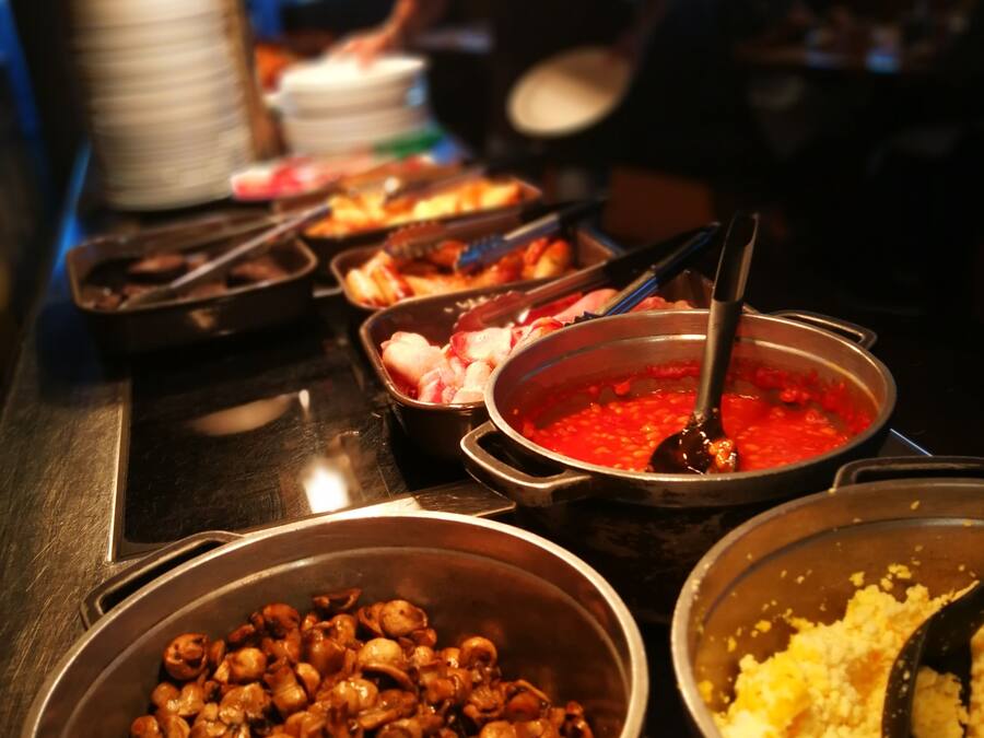 Un bufé con diversos platos, incluyendo una olla de salsa roja, un tazón de champiñones y una fuente de arroz amarillo.
