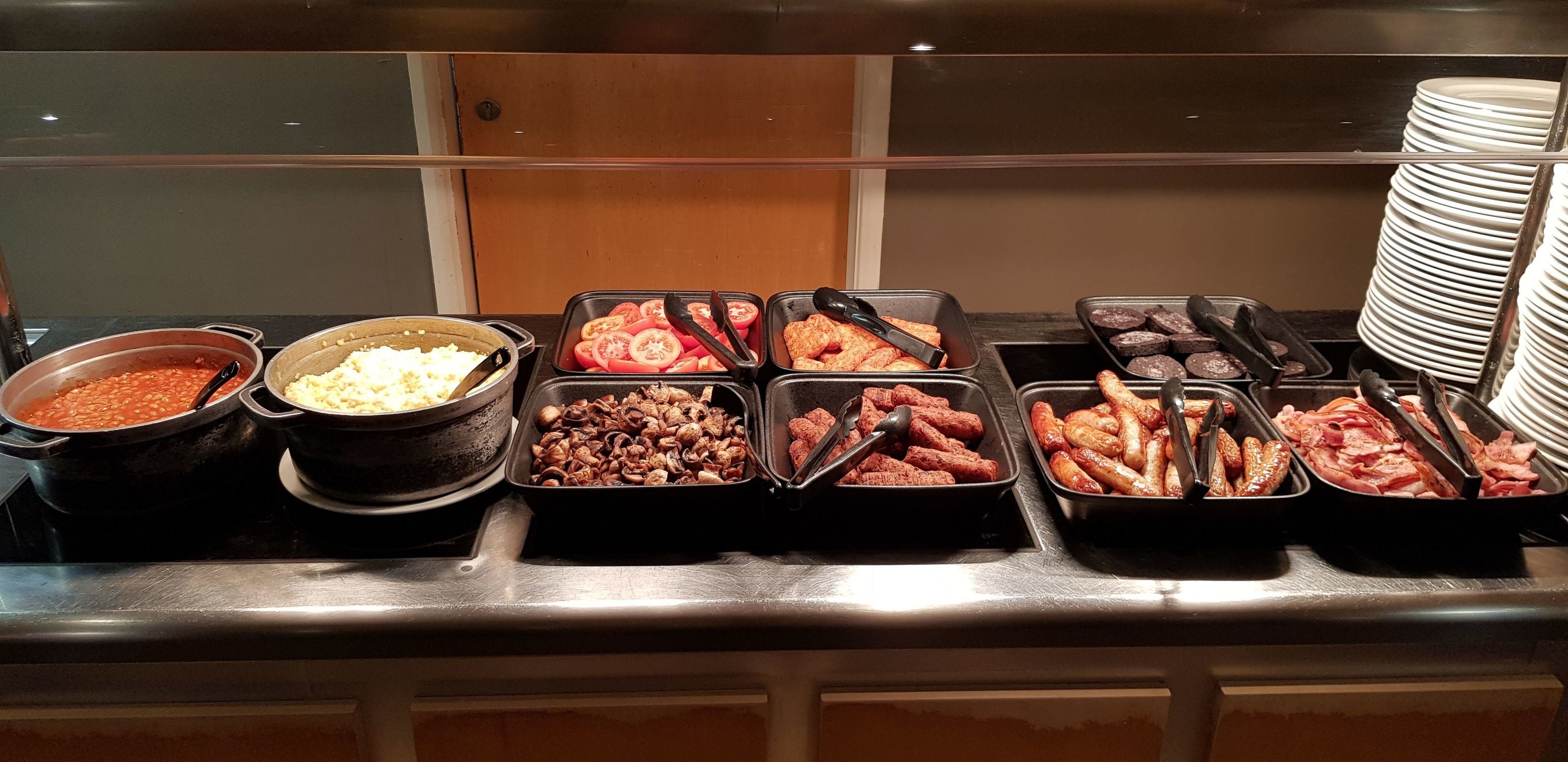 A buffet with various food options including beans, sausages, and sliced tomatoes.