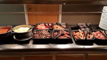A buffet with various food options including beans, sausages, and sliced tomatoes.