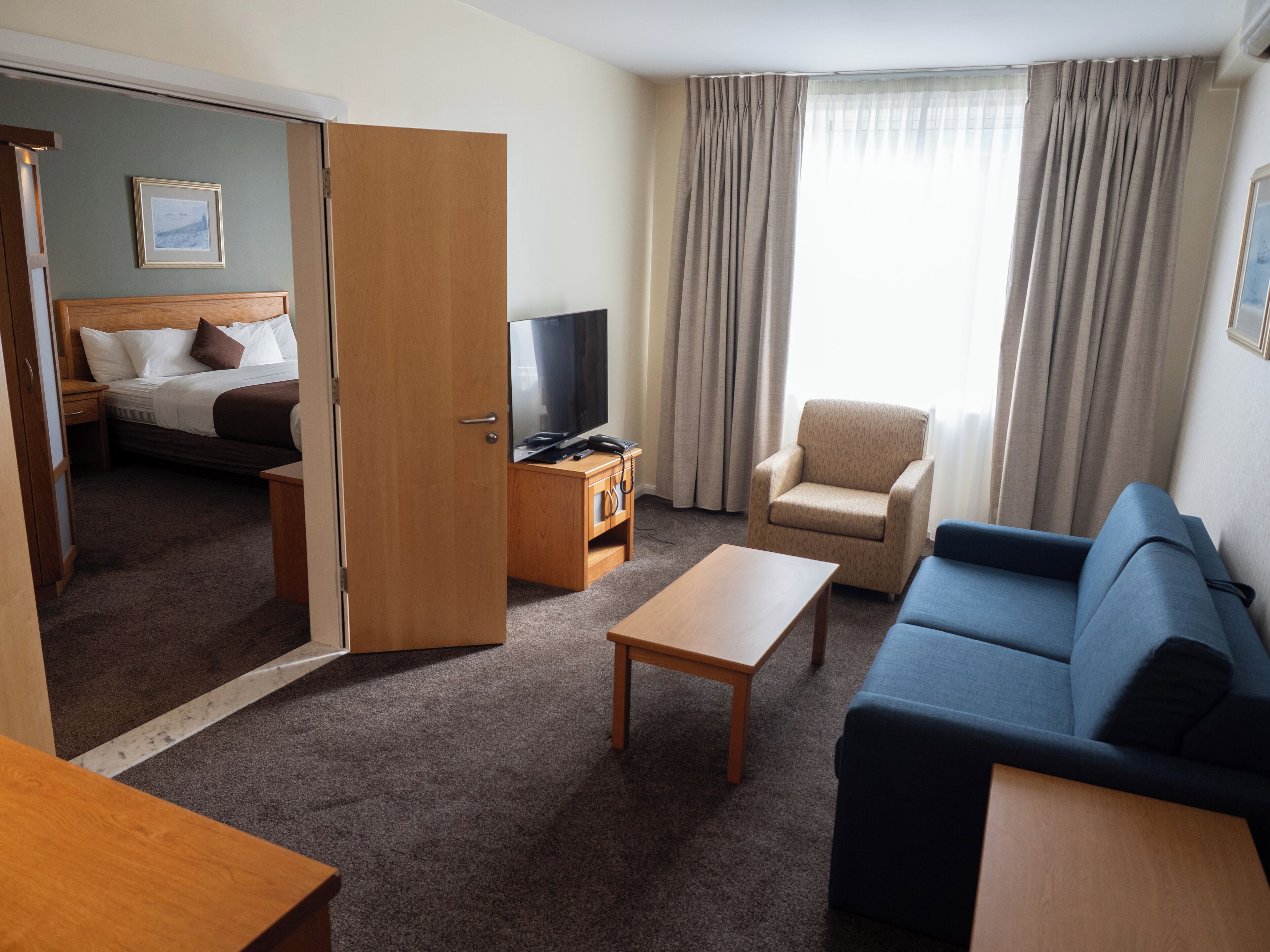 A hotel room with a bed, a TV, a sofa, a chair, and a small table.