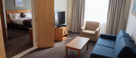 Een hotelkamer met een bed, een televisie, een bank, een stoel en een klein tafeltje.