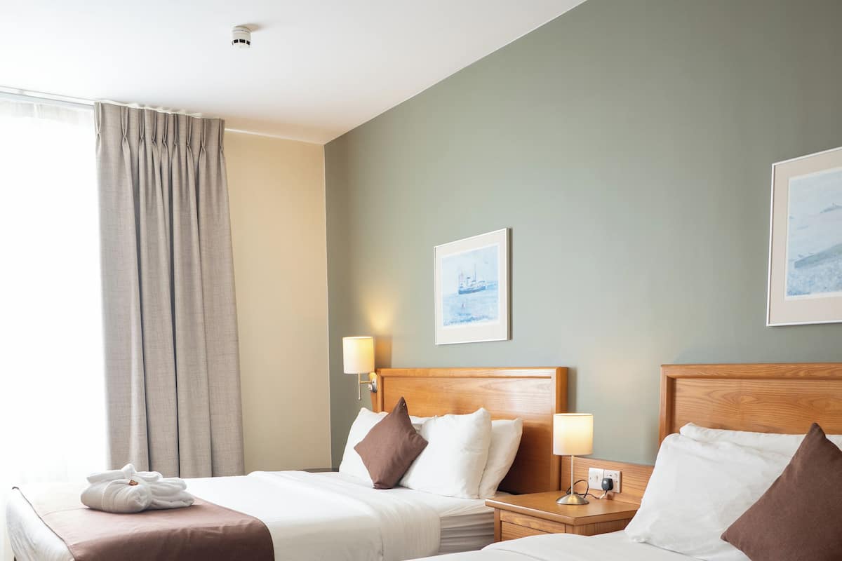 A hotel room with two beds, a nightstand, a lamp, and a framed picture on the wall.