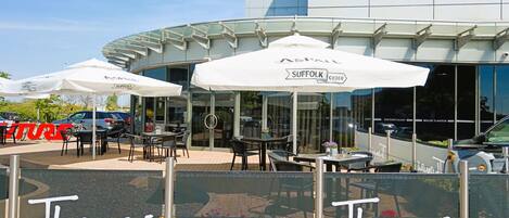 An outdoor seating area with tables and chairs under umbrellas, a modern building in the background, and a glass barrier with the name "Thomas Restaurant and Bar" on it.