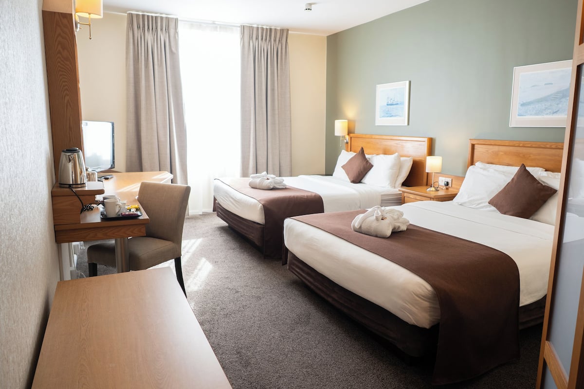 A hotel room with two beds, a desk, a chair, and a window with curtains.