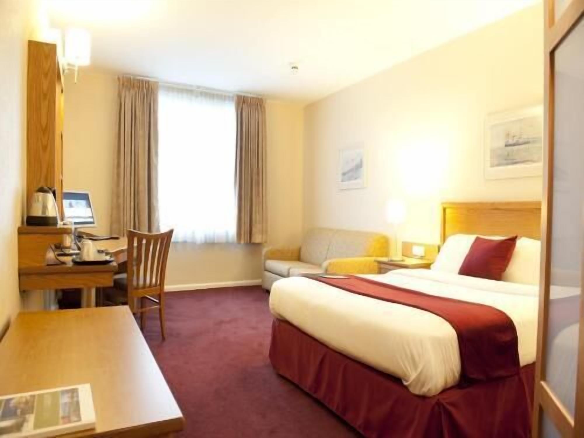 A hotel room with a bed, desk, chair, and a window with curtains.