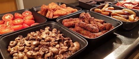 Un buffet proposant une variété de plats, notamment des tomates en tranches, des champignons et des saucisses.