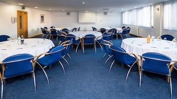 A conference room with round tables, blue chairs, and white tablecloths.