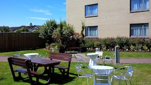 An outdoor patio area with a wooden bench, metal chairs, and a small round table.