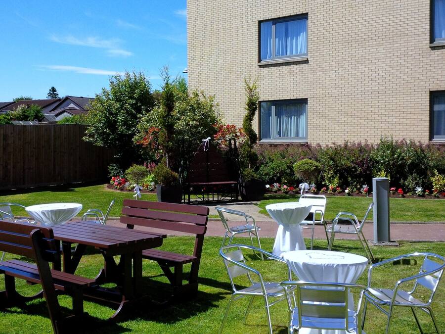 An outdoor patio area with a wooden bench, metal chairs, and a small round table.