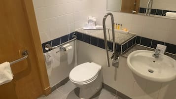Un baño con inodoro, lavamanos y barras de apoyo.