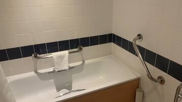 A standard hotel bathroom with a bathtub, a handrail, and a towel rack.