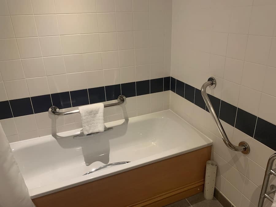 A standard hotel bathroom with a bathtub, a handrail, and a towel rack.