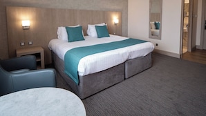 A hotel room with a large bed, a desk, a chair, and a round table.