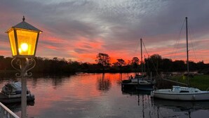 Une rivière paisible au coucher du soleil, avec des bateaux amarrés, un lampadaire et un ciel dégagé.
